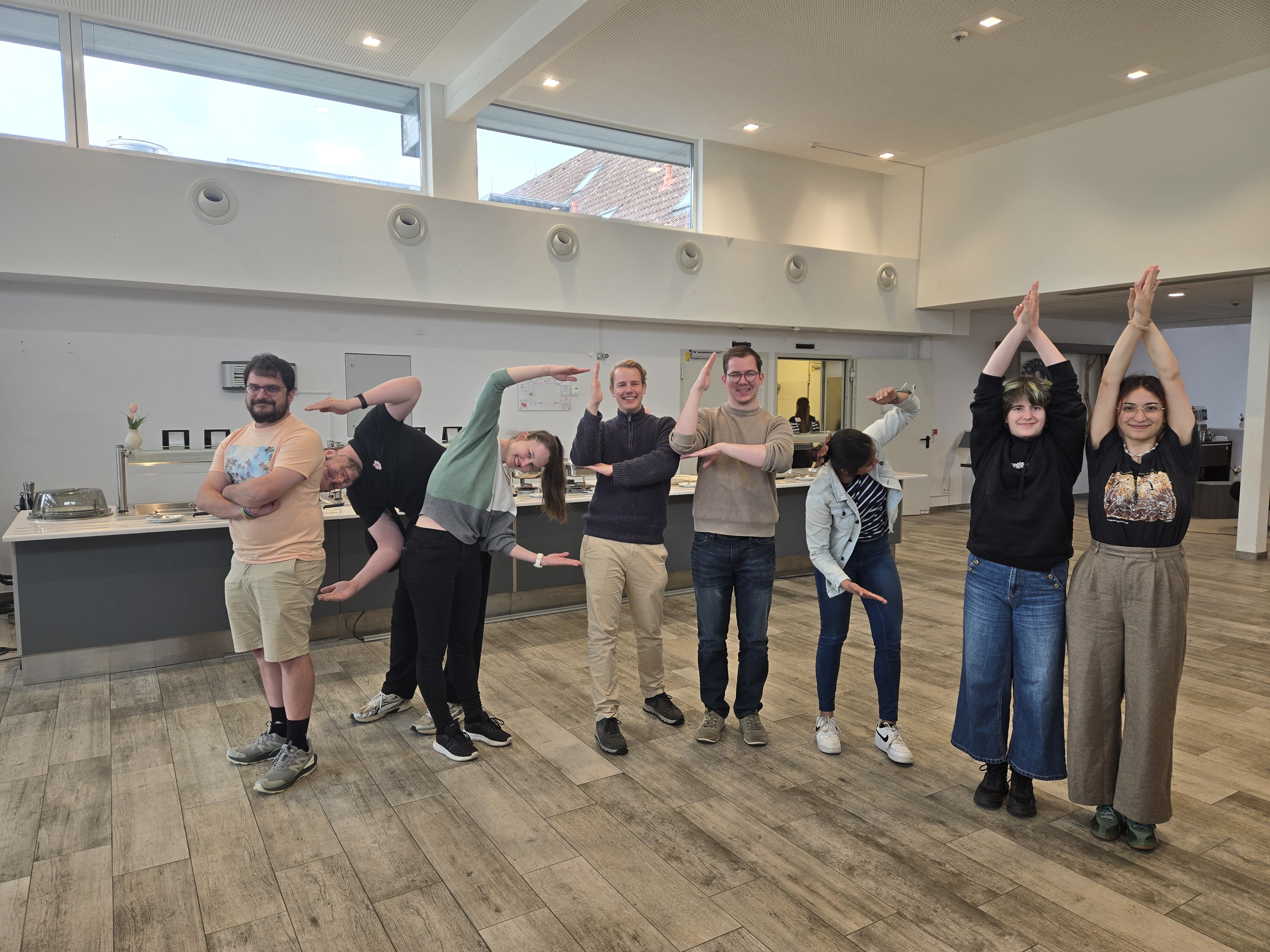 Physiker posieren mit lustigen, yoga-&auml;hnlichen Posen in einer modernen Cafeteria.